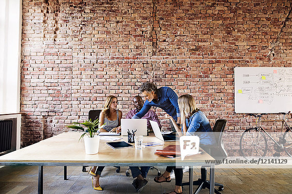 Geschäftsleute mit Laptops diskutieren am Schreibtisch im Büro