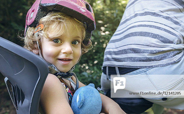 Portrait of little girl with helmet sitting on a child seat for bicycle with her father