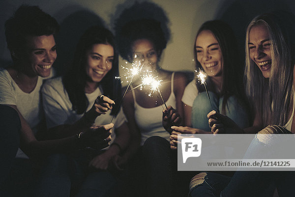 Happy female friends with sparklers in the dark