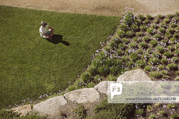 Mann mit VR-Brille sitzend auf Rasen im Garten