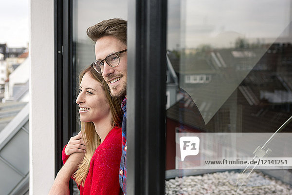 Lächelndes junges Paar schaut aus dem Fenster