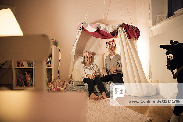 Portrait von zwei glücklichen Mädchen mit Tablette im Kinderzimmer