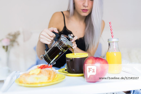 Young woman having breakfast in bed pouring coffee into cup