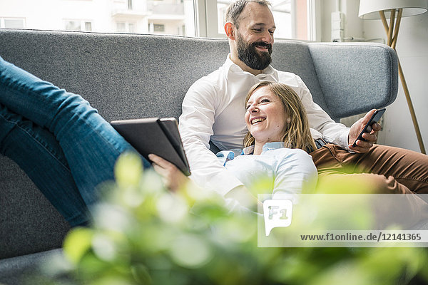 Smiling couple using tablet and cell phone on couch