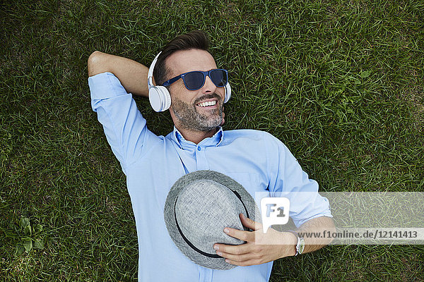 Porträt eines lachenden Mannes  der sich auf einer Wiese entspannt und Musik mit Kopfhörern hört  Draufsicht