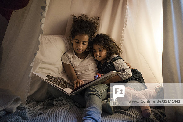 Two sisters sitting in dark children's room  reading a book