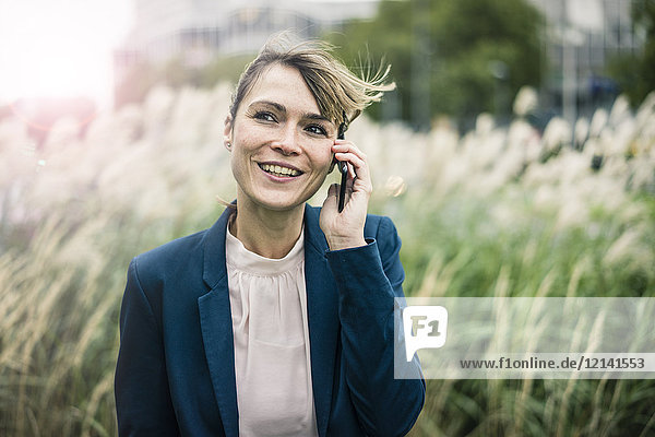Lächelnde Geschäftsfrau am Handy im Freien
