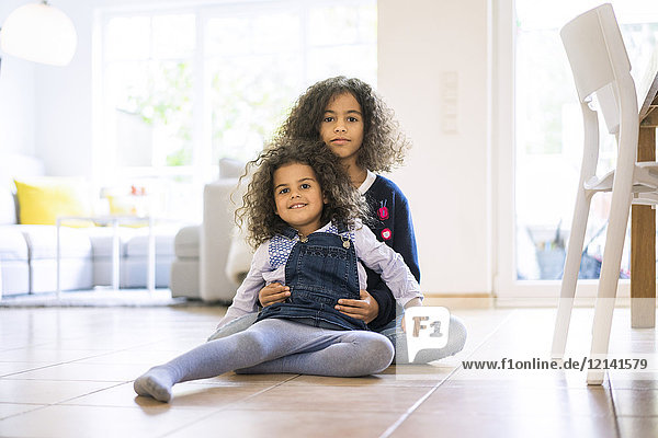 Little girl sitting on floor in living room  holding her sister  portrait