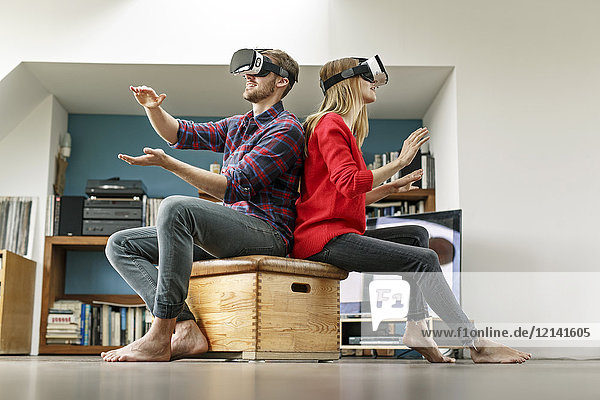 Junges Paar zu Hause auf Box sitzend mit VR-Brille