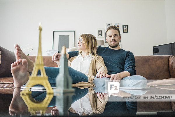Couple sitting on couch at home with model of Eiffel Tower and Empire State Building