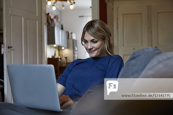 Porträt einer lächelnden Frau mit Laptop auf der Couch zu Hause
