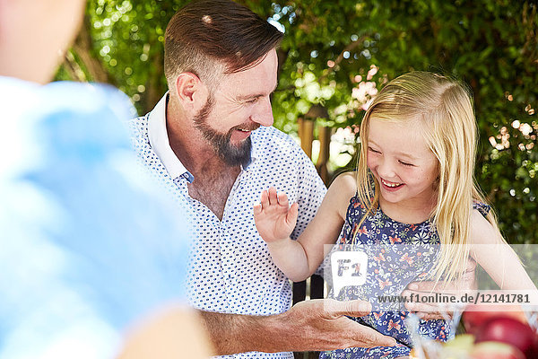 Happy girl with father sitting at garden table high fiving