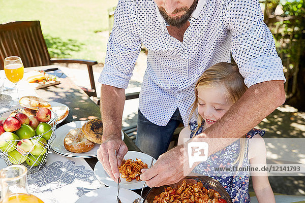 Father dishing up pasta for daughter at garden table
