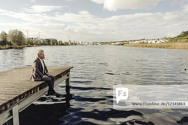 Älterer Mann sitzt auf einem Steg am See