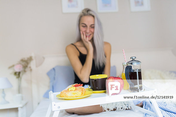 Smiling young woman having breakfast in bed