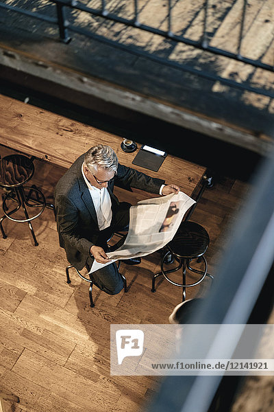 Senior Geschäftsmann sitzt im Café und liest Zeitung.