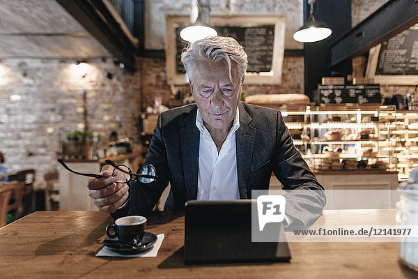 Senior Geschäftsmann sitzend im Cafe  mit digitalem Tablett  Lesen