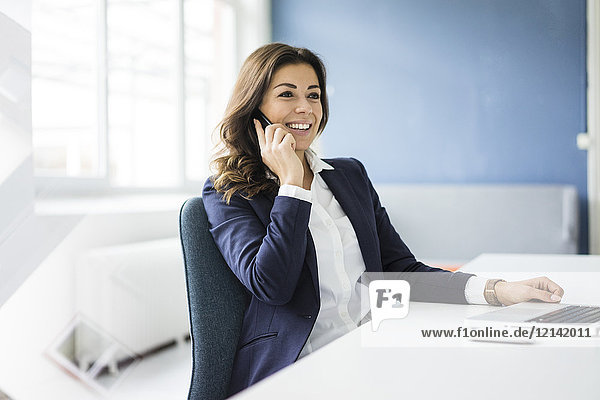Porträt einer lächelnden Geschäftsfrau am Telefon am Schreibtisch im Büro