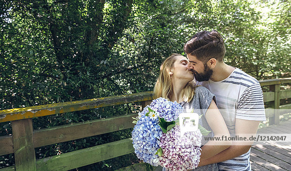 Couple with with a bouquet of hydrangeas kissing on a wooden walkway in the countryside