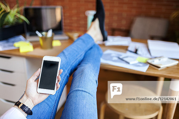 Nahaufnahme einer Geschäftsfrau  die ein Handy mit Füßen auf dem Tisch im Büro hält.