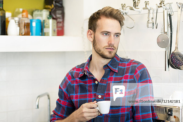 Nachdenklicher junger Mann mit Tasse Espresso in der Küche zu Hause