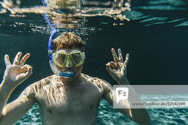 Porträt eines Mannes mit Taucherbrille und Schnorchel unter Wasser in einem Schwimmbad.