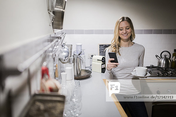 Smiling woman checking cell phone in kitchen