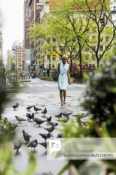USA  New York  junge blonde Afroamerikanerin auf der Straße  Tauben