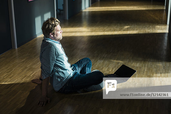 Geschäftsmann mit Laptop im Büro auf dem Boden sitzend