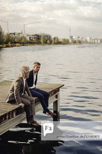 Two businessmen sitting on jetty at a lake