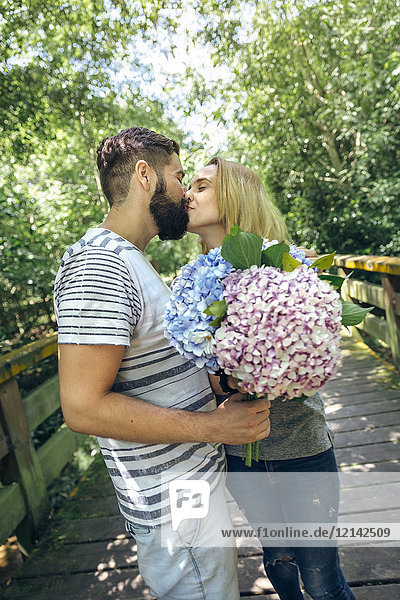 Couple with with a bouquet of hydrangeas kissing on a wooden walkway in the countryside