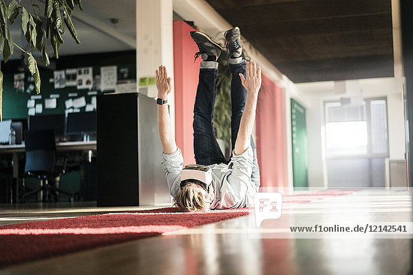 Businessman lying on carpet on the floor wearing VR glasses exercising
