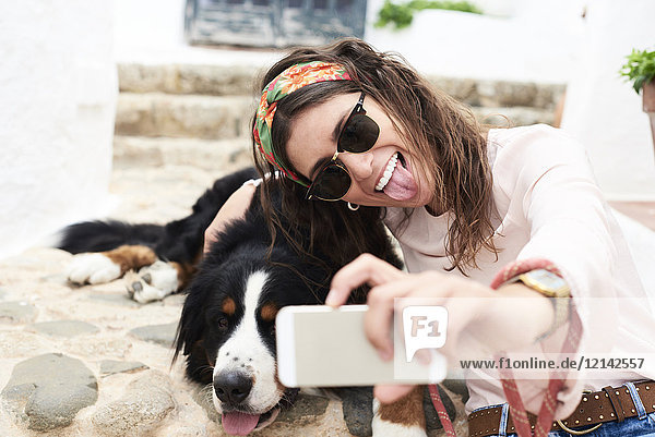 Brünettes Mädchen nimmt Selfie  müde Berner Sennenhund auf dem Boden liegend