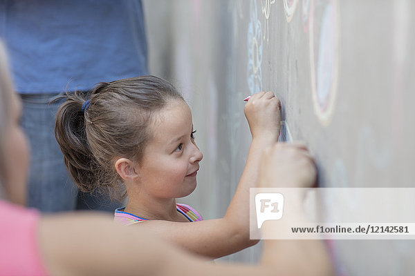 Mädchen beim Zeichnen von bunten Bildern mit Kreide auf einer Betonwand