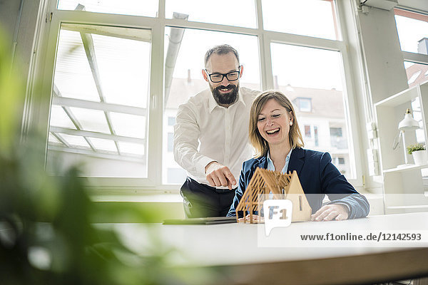 Laughing woman and man with house model in office