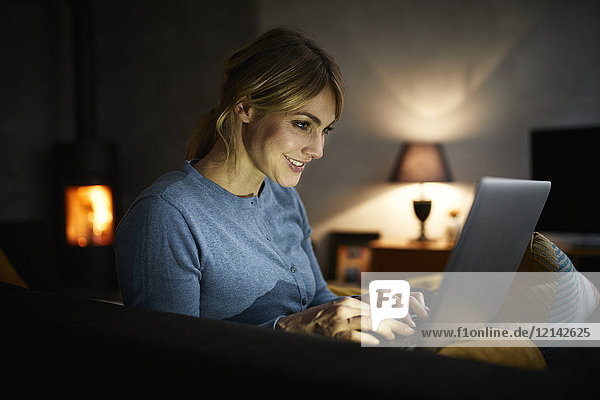 Lächelnde Frau mit Laptop zu Hause am Abend