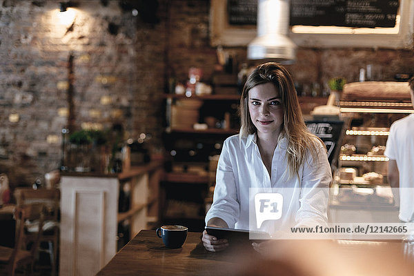 Lächelnde blonde Frau sitzt im Cafe  mit Tablette