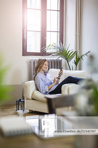 Smiling woman on couch at home holding phone