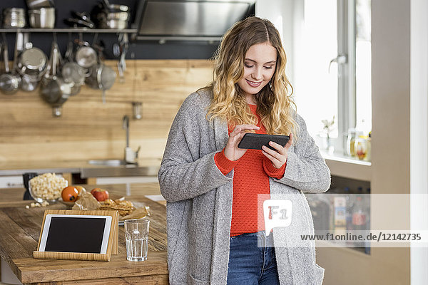Portrait of smiling young woman using smartphone in the kitchen