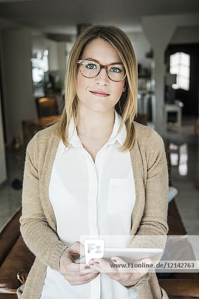 Portrait of smiling woman holding tablet at home