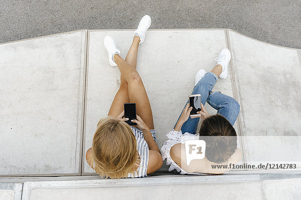 Zwei junge Frauen  die Handys in einem Skatepark benutzen.