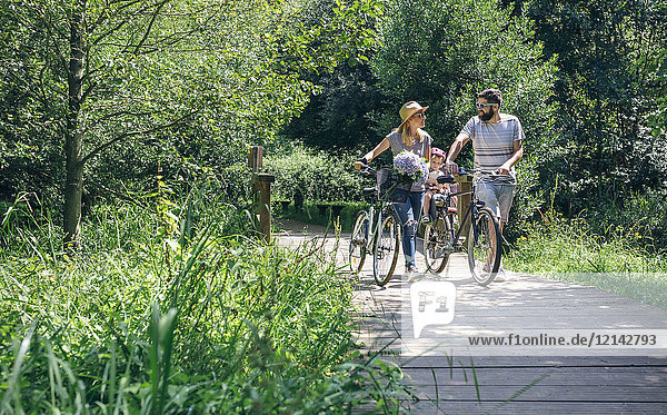 Family pushing bicycles on wooden walkway