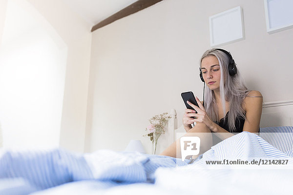 Junge Frau im Bett mit Handy und Kopfhörer