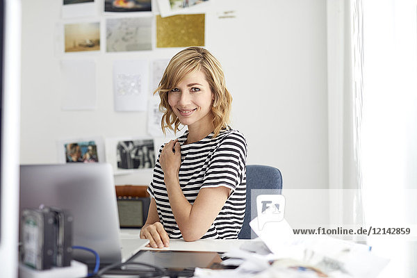 Portrait of smiling blond business woman with laptop  sitting at desk