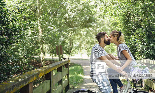 Couple with bicycle kissing on a wooden walkway in the countryside