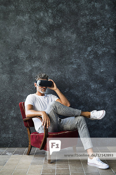 Erwachsener Mann  der durch die VR-Brille schaut  im Sessel sitzend
