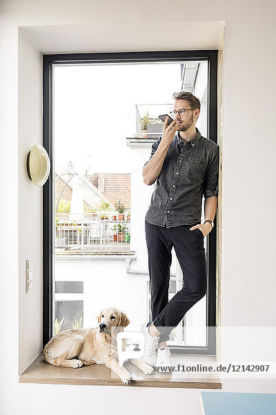 Mann mit Smartphone am Fenster neben dem Hund