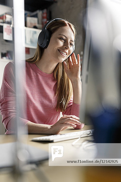 Lächelnde junge Frau mit Kopfhörer am Schreibtisch zu Hause