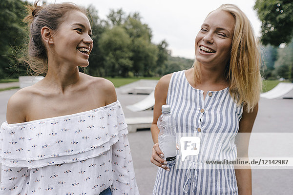 Zwei lachende junge Frauen mit einer Flasche Wasser im Freien.