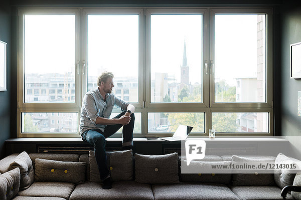 Businessman sitting at the window in lounge area of an office